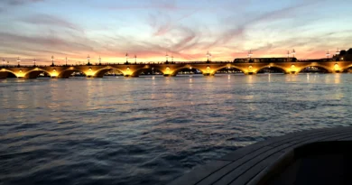 Vue du Pont de Pierre à Bordeaux au coucher de soleil avec des lumières illuminant les arches et le reflet sur la Garonne.